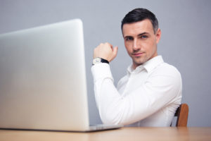 Businessman sitting at the table with laptop and looking at camera after writing awesome piece of marketing content