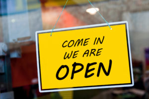 come in we are open sign hanging on a window door outside a local business trying to drive online customers in